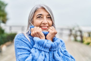 Orta yaşlı, kır saçlı, gülümseyen, kendine güvenen bir kadın.
