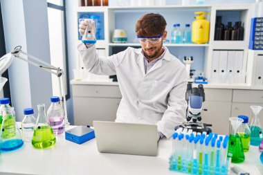 Young arab man scientist using laptop measuring liquid at laboratory