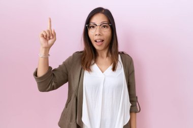 Pembe arka planda gözlük takan orta yaşlı Çinli kadın başarılı bir fikirle işaret ediyor. Heyecanlı ve mutlu. Bir numara.. 