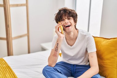 Genç İspanyol adam akıllı telefonda konuşuyor. Yatak odasında oturuyor.