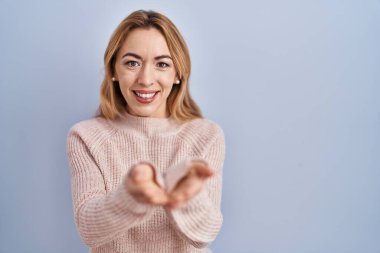 Hispanic woman standing over blue background smiling with hands palms together receiving or giving gesture. hold and protection 