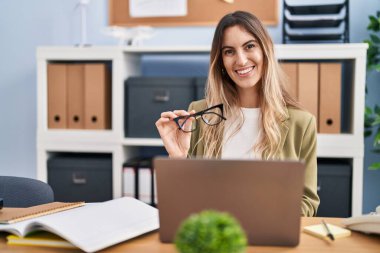 Young woman business worker using laptop holding glasses at office