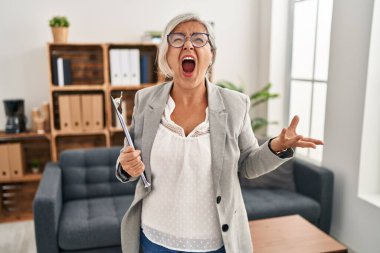Muayenehanedeki gri saçlı, sinirli ve kızgın çığlık atan öfkeli, öfkeyle bağıran orta yaşlı bir kadın. öfke ve agresif konsept. 