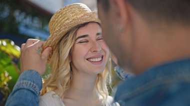 Erkek ve kadın çift parkta yaz şapkası takarak gülümsüyor.