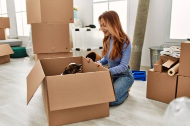 Genç beyaz kadın, yeni evinde yerde oturan köpeğe bakıyor.