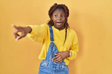 Sarı arka planda dikilen Afrikalı kadın parmağı önde şaşırmış, ağzı açık şaşırmış, ön tarafta bir şey var. 