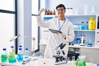 Young hispanic man scientist holding test tube with plant at laboratory clipart