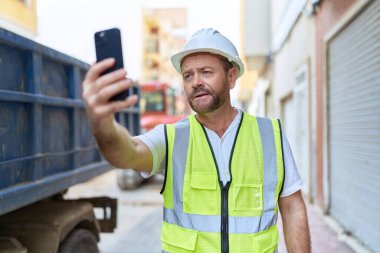 Orta yaşlı bir mimarın sokakta video görüşmesi var.