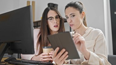 İki kadın işçi dokunmatik ped kullanıyor. Ofiste kahve içiyor.