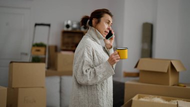 Orta yaşlı İspanyol kadın akıllı telefondan konuşuyor. Yeni evinde kahve içiyor.