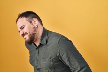 Ayrıca, sarı arka planda duran, sırt ağrısı çeken, elleriyle dokunan, kaslı, iri yarı, İspanyol sakallı adam. 