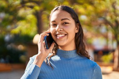 Genç Afrikalı Amerikalı kadın gülümsüyor. Parktaki akıllı telefondan konuşuyor.