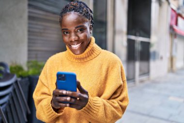 Afro-Amerikalı kadın sokakta akıllı telefon kullanarak kendine güveniyor.