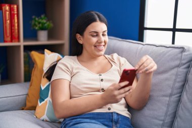 Evdeki kanepede oturan akıllı telefon kullanan genç, güzel İspanyol kadın.