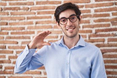 Duvarın arkasında duran İspanyol asıllı genç adam gülümsüyor ve el hareketleriyle hareket ediyor parmaklarıyla işaret yapıyor ve kameraya bakıyor. ölçüm kavramı. 