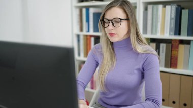 Young blonde woman student using computer studying at library university