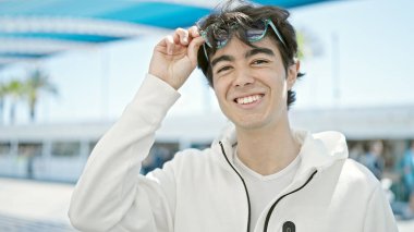 Young hispanic man smiling confident wearing sunglasses at park