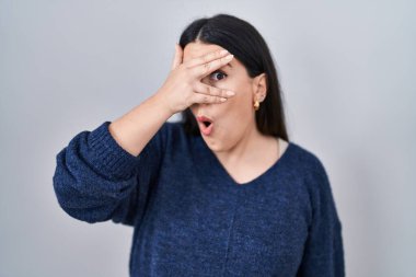 Genç esmer kadın izole edilmiş arka planda duruyor. Şoka giriyor. Yüzü ve gözleri kapanıyor, utangaç ifadesiyle parmaklarından bakıyor.. 