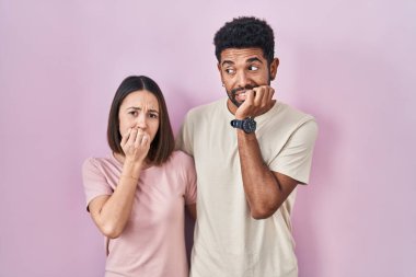 Pembe arka planda genç bir İspanyol çift. Elleri ağız ısıran tırnaklarıyla stresli ve gergin görünüyorlar. anksiyete. 