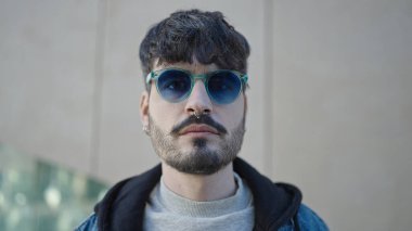 Sokağın ortasında güneş gözlüğü takmış, ciddi bir ifadeyle duran İspanyol genç adam.