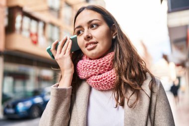 Genç, güzel, İspanyol bir kadın sokakta atkı takarak akıllı telefondan sesli mesaj dinliyor.