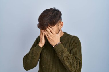 Arab man with beard standing over blue background with sad expression covering face with hands while crying. depression concept. 