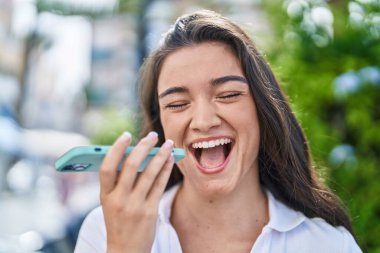 Genç İspanyol kadın gülümsüyor. Parkta akıllı telefondan konuşuyor.