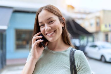 Genç, güzel bir kadın, gülümsüyor. Kendine güveniyor. Akıllı telefondan konuşuyor.