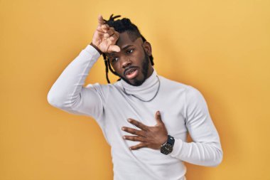 Sarı arka planda balıkçı yaka kazak giyen Afrikalı adam hastalık ve ateş için alnına dokunuyor, grip ve soğuk algınlığı, virüs hastalığı. 