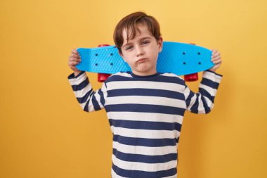 Sarı arka planda paten tutan küçük beyaz çocuk yüzünde ciddi bir ifadeyle rahatladı. Basit ve doğal bir şekilde kameraya bakıyorsun.. 