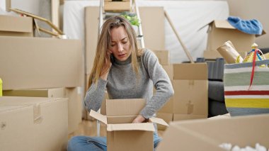 Karton kutuları açan beyaz bir kadın telefonda konuşuyor. Yeni evde şikayet ediyor.