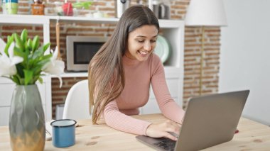 Yemek odasındaki masada dizüstü bilgisayar kullanan güzel İspanyol kadın.