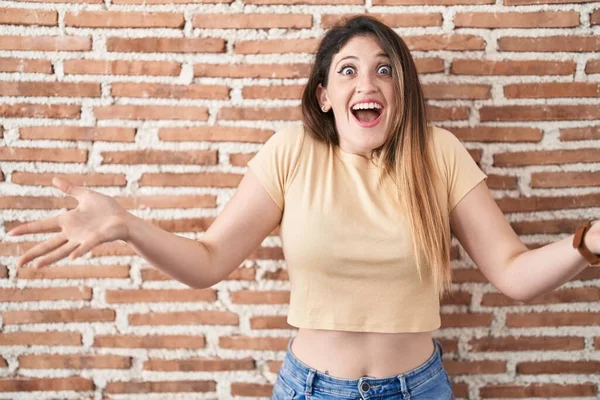 レンガの壁に立っている若いブルネットの女性は狂気を祝い 腕を上げて興奮して叫んで目を開けて成功に驚いています 勝者のコンセプト — ストック写真