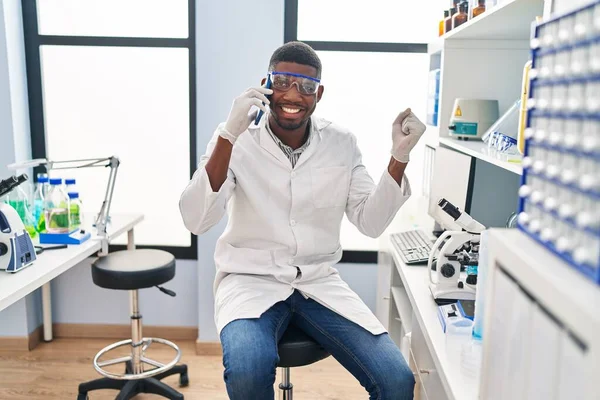 アフリカ系アメリカ人の男性科学者の研究室で働いている電話で話すことは誇りに思って叫んで勝利と成功を祝う非常に興奮して腕を上げ — ストック写真