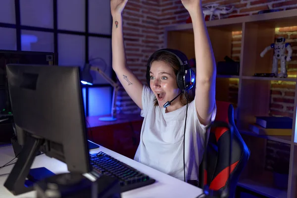 Young caucasian woman streamer playing video game with winner expression at gaming room