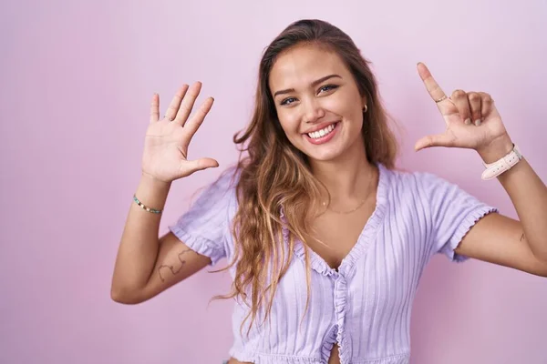 年轻的惊慌失措的女人站在粉红的背景上 带着自信和快乐的微笑 用七号手指指指着 — 图库照片