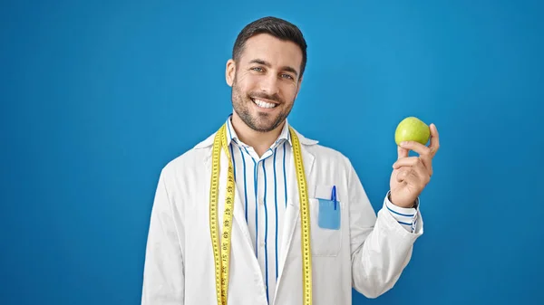 Joven Hombre Hispano Dietista Sonriendo Confiado Sosteniendo Manzana Sobre Aislado —  Fotos de Stock