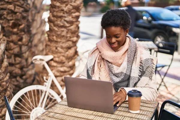 African american woman using laptop drinking coffee sitting on table at coffee shop terrace