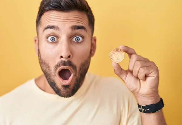 stock image Handsome hispanic man holding tron cryptocurrency coin scared and amazed with open mouth for surprise, disbelief face 