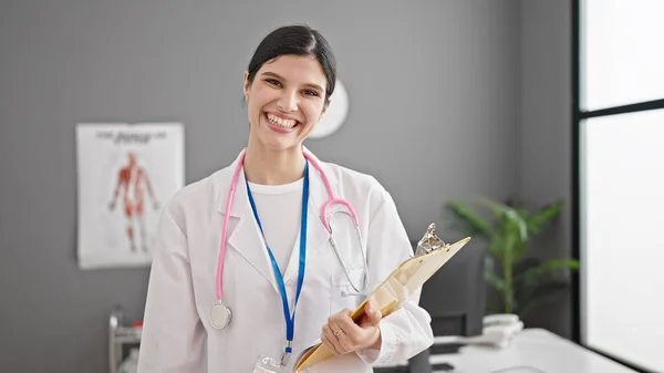 年轻美丽的惊慌失措的女医生微笑着 自信地拿着剪贴板站在诊所 — 图库照片