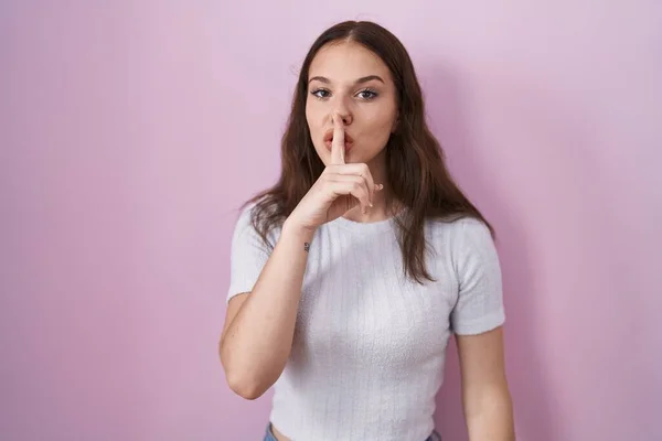 年轻的惊慌失措的女孩站在粉色的背景上 要求安静 手指放在嘴唇上 沉默和秘密概念 — 图库照片