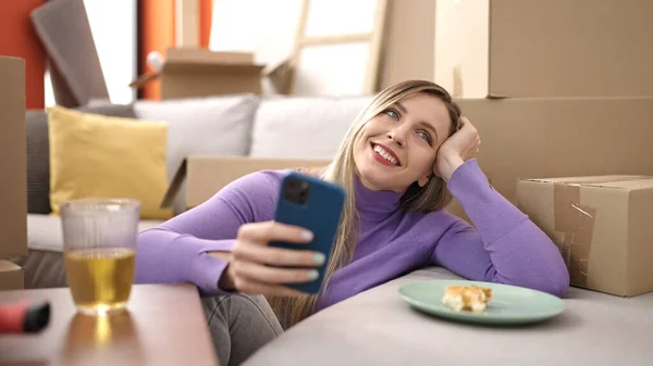 若いですブロンド女性使用してスマートフォン座っている上の床に新しい家 — ストック写真