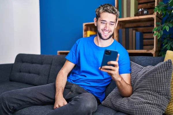 使用智能手机 坐在家里的沙发上的年轻人 — 图库照片