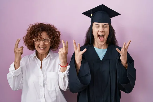 卒業キャップと儀式用のローブを着たヒスパニック系の母親と娘は 腕を上げて興奮して叫んで目を閉じて成功のために狂気と狂気を祝います 勝者のコンセプト — ストック写真