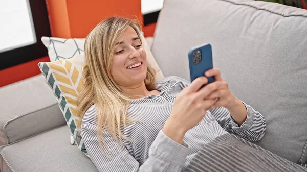 Jovem Loira Usando Smartphone Deitado Sofá Casa — Fotografia de Stock