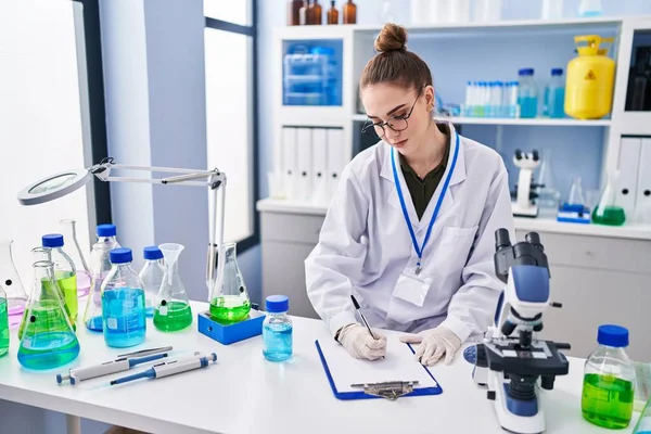 stock image Young woman scientist measuring liquid writing on document at laboratory