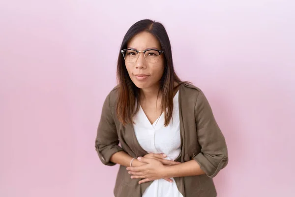 中年妇女因消化不良 病痛而戴眼镜 背带粉色背景 双手放在肚子上 疼痛的概念 — 图库照片