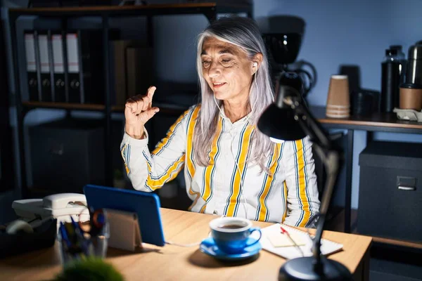 夜のオフィスで働く白髪の中年女性は笑顔で 指を見てカメラで小さなサイズの看板をして手で自信を持ってジェスチャー 概念を測定し — ストック写真
