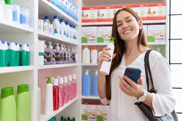 在药店用智能手机拿着洗发水瓶的年轻美女顾客 — 图库照片