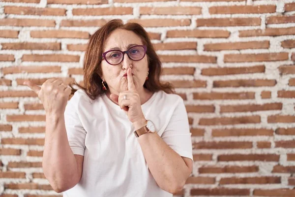 站在砖墙上戴眼镜的老妇人要求安静 手指放在嘴唇上 手放在旁边 沉默和秘密概念 — 图库照片